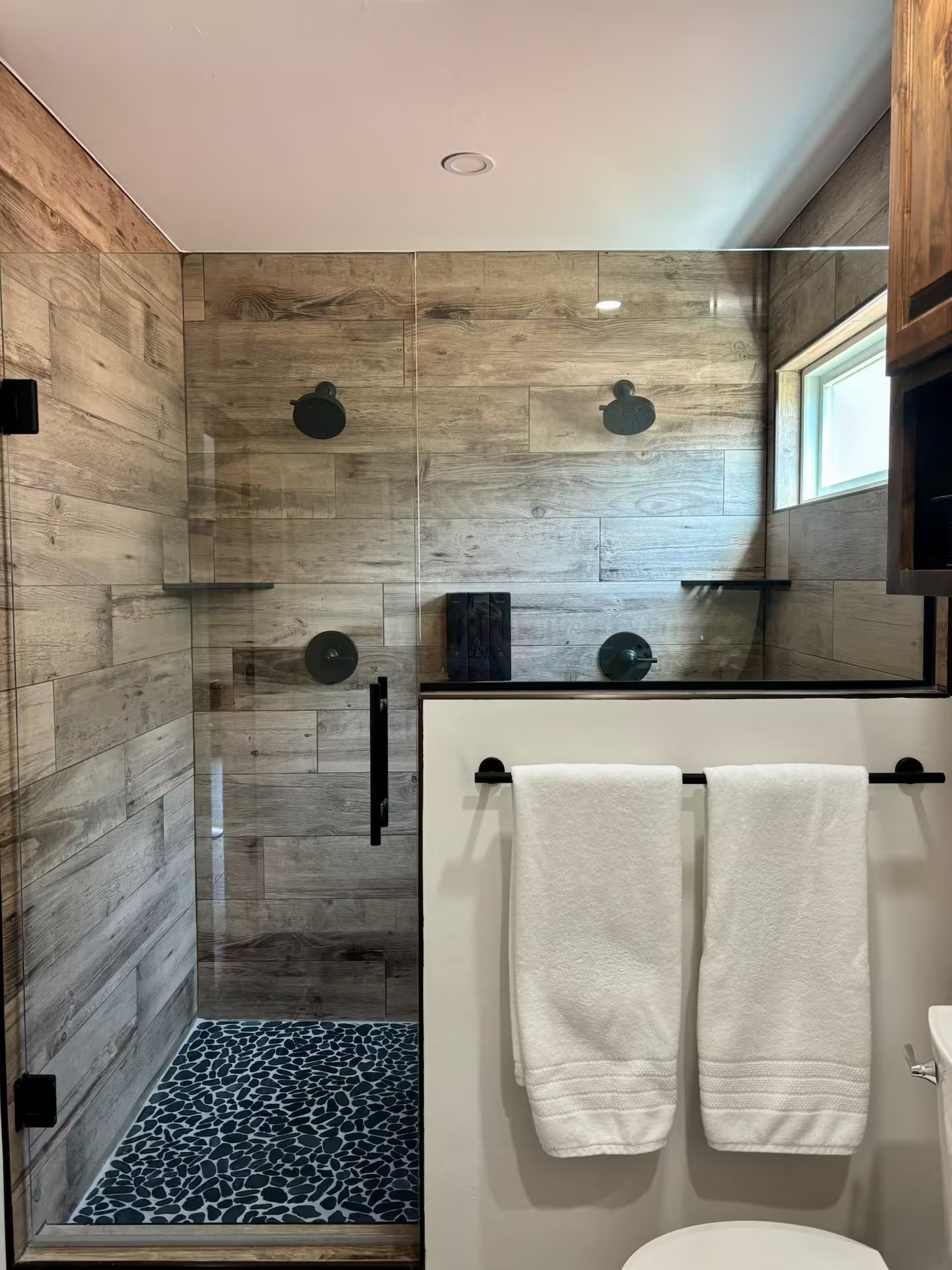 A modern bathroom with a glass shower enclosure, wooden wall tiles, and a white toilet.