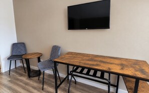 Una habitación con una mesa de madera, dos sillas y un televisor montado.