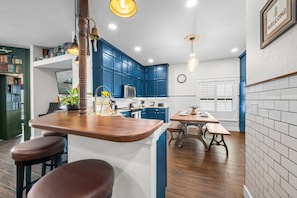 A modern kitchen with blue cabinets, a wooden island with stools, and a dining table with benches. - Indiana Jones & Jungle Cruise • Genuine Disney Décor • Secret Bookcase • Pool (Clermont)