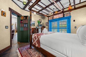 Une chambre avec un grand lit, une bibliothèque verte, une porte bleue et une vue par la fenêtre.