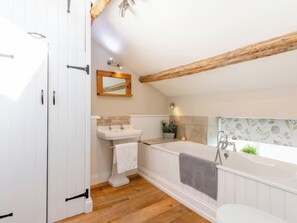 A bathroom with a white sink, a bathtub, and a wooden ceiling beam. - The Quirky Cottage (Penrith)