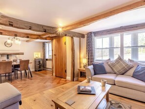 A cozy living room with a wooden floor, a sofa, a coffee table, and a dining area with chairs and a table. - The Quirky Cottage (Penrith)