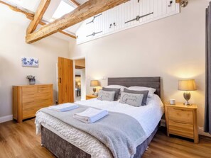 A bedroom with a bed, bedside tables, a dresser, and a door. - The Quirky Cottage (Penrith)
