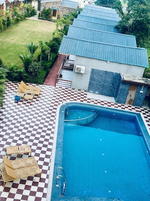 A swimming pool with checkered flooring, lounge chairs, and a small building with a blue roof. - The Dhela Jungle Resort (Dhela)