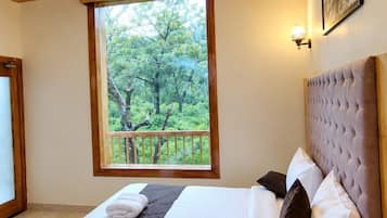 A bedroom with a bed, a ceiling fan, a window with a view, and a wall-mounted light fixture.