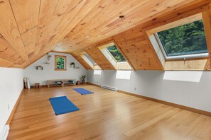 A spacious attic room with wooden floors, skylights, and a view of the forest.