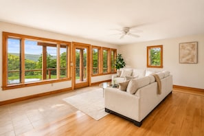 Ein geräumiges Wohnzimmer mit großem Fenster, Deckenventilator und beiger Couch.