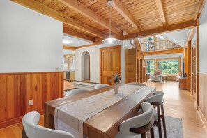 A spacious dining area with a wooden table and chairs, a view of the kitchen, and a loft space with a balcony.