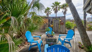 Eine Holzterrasse mit blauen Stühlen, einem kleinen Tisch und einem dekorativen Zaun mit Sonnenblumen und einer Holztür.