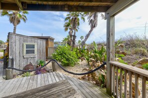 Une terrasse en bois avec une barrière en corde, une petite structure en bois et une végétation tropicale.