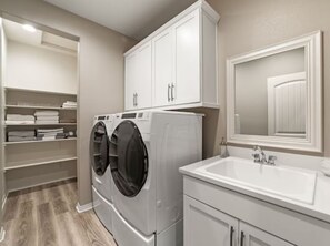 A laundry room with a washing machine, dryer, and a sink with a mirror above it. - South-Facing La Quinta Pool Home with Stunning Mountain & Sunset Views (La Quinta)