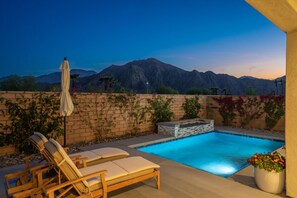 A swimming pool with lounge chairs and a hot tub, surrounded by a brick wall and plants, with mountains in the background. - South-Facing La Quinta Pool Home with Stunning Mountain & Sunset Views (La Quinta)