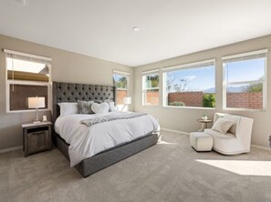 A bedroom with a large bed, a nightstand, a sofa, and a window with a view. - South-Facing La Quinta Pool Home with Stunning Mountain & Sunset Views (La Quinta)