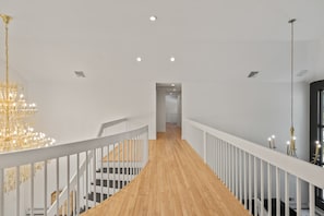 Un interior moderno con una escalera de madera, barandillas blancas y una araña.