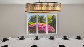 Un comedor con una mesa dispuesta para una comida, un amplio ventanal con vistas a flores rosadas y una lámpara colgante moderna.