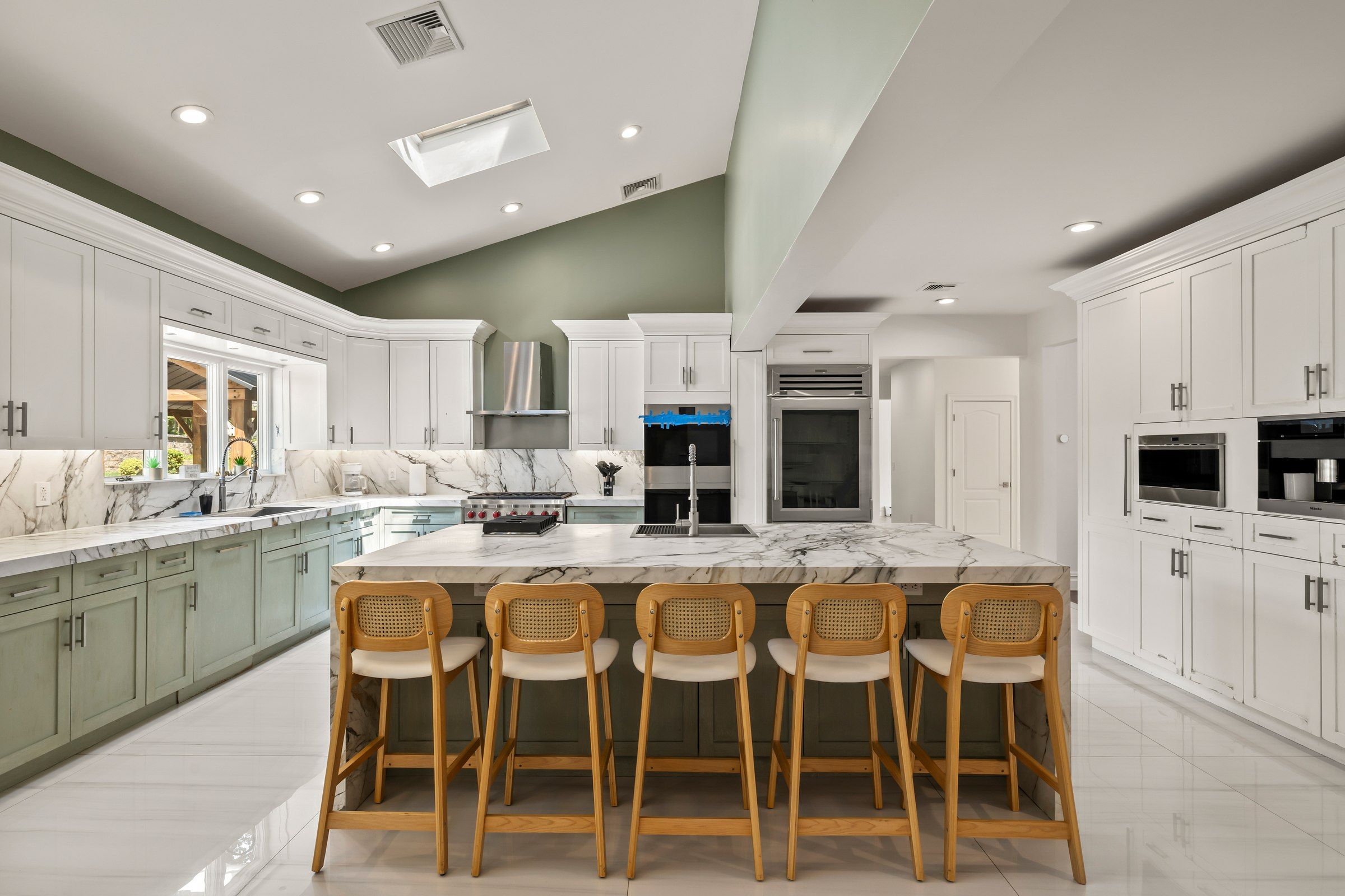 Cocina moderna con encimera de mármol, electrodomésticos de acero inoxidable y una isla central con taburetes de bar.
