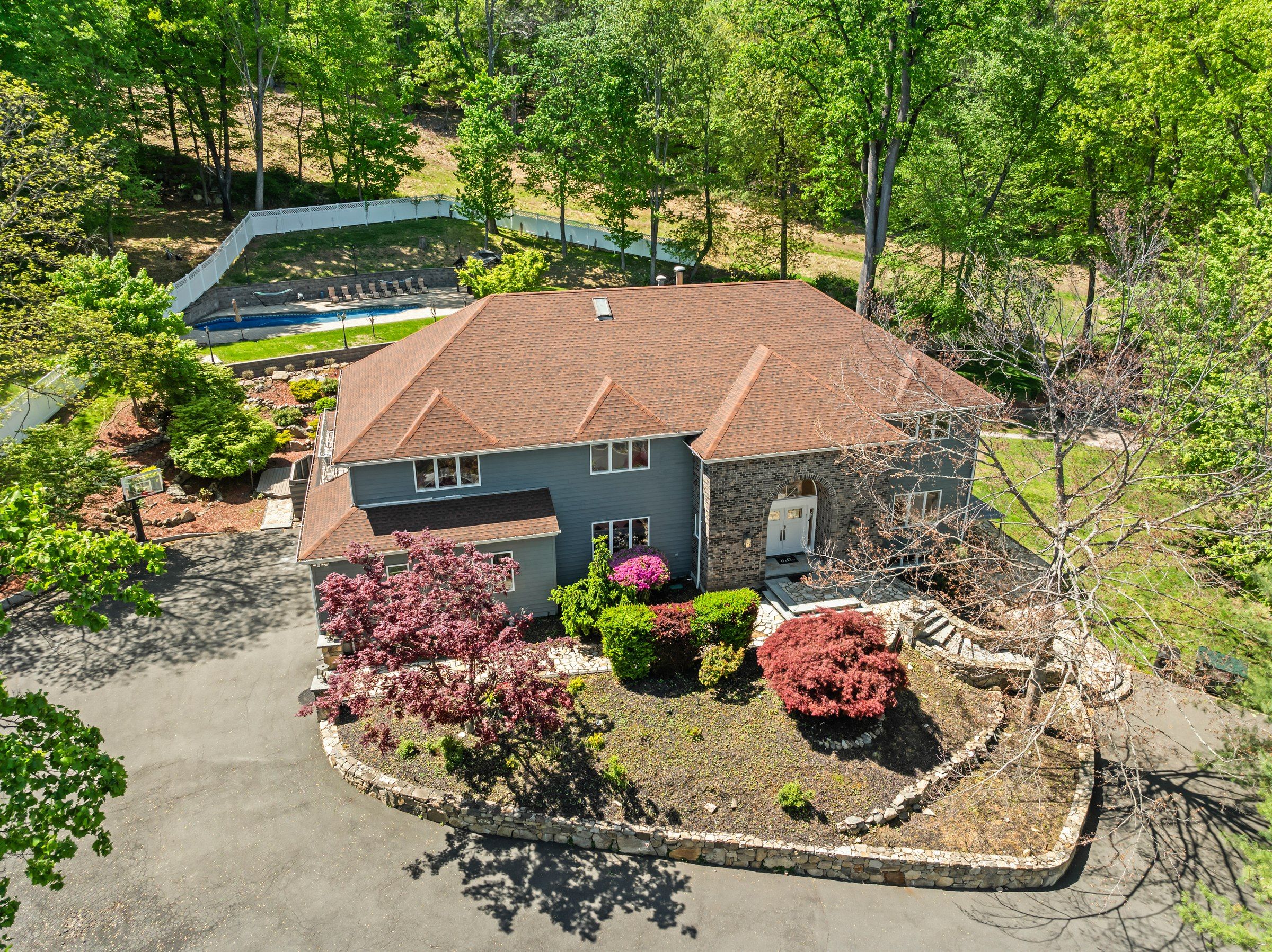 A two-story house with a brick roof, a front porch, and a swimming pool in the background.