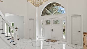 A spacious lobby with a grand chandelier, a staircase, and a large arched doorway.
