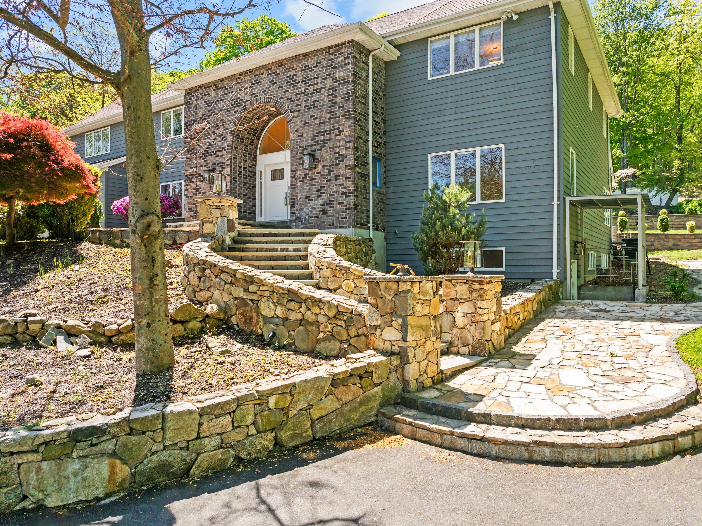Una casa de dos plantas con una escalera de piedra que lleva a la puerta principal, un muro de contención de piedra y un patio de piedra circular.