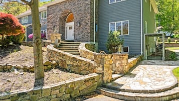 Una casa de dos plantas con una escalera de piedra que lleva a la puerta principal, un muro de contención de piedra y un patio de piedra circular.