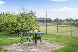 A patio with a table and chairs, a vase with flowers, and a view of a sports field through a fence. - 2 Bed in York (oc-y008) (Gilling East)