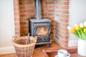 A brick fireplace with a modern wood-burning stove, a wicker basket, and a vase with flowers. - 2 Bed in York (oc-y008) (Gilling East)