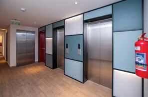 A hallway with three elevators, a fire extinguisher, and a door with a red handle. - Spacious Living, Pool & Workspace, Near Shopping (Asunción)