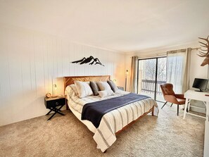 A bedroom with a bed, bedside table, lamp, chair, desk, and a large window. - Renovated 2BR Mountain View Condo ½ Mile to Beech Mtn Resort (Beech Mountain)