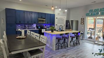 Une cuisine moderne avec des meubles de couleur bleu foncé, un îlot central doté de tabourets, une table à manger avec des chaises et un réfrigérateur.