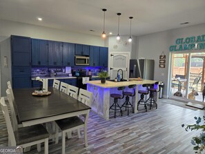 Una cucina moderna con mobili blu scuro, un'isola centrale con sgabelli da bar, un tavolo da pranzo con sedie e un frigorifero.