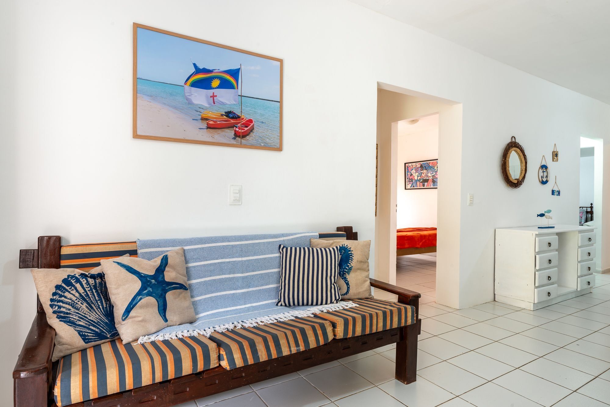 Un salon avec un canapé, des coussins, un tableau et un couloir menant à une autre pièce.