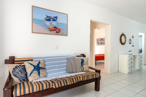 A living room with a sofa, pillows, a painting, and a hallway leading to another room.