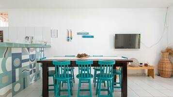 Cozinha moderna com área de refeições, piso de azulejos brancos, mesa de madeira com quatro cadeiras e televisão de tela plana na parede.