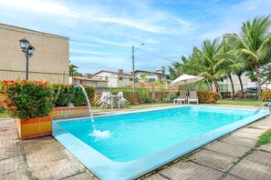 A swimming pool with a tiled edge, surrounded by a fence, with a chair and umbrella nearby.