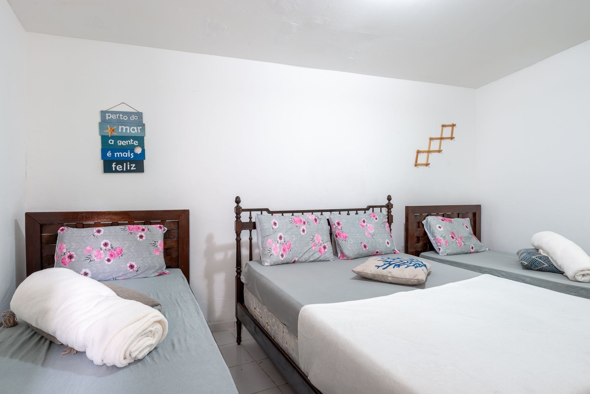 Une chambre d’hôtel avec deux lits, une tête de lit en bois, des coussins à motifs floraux et une décoration murale avec une phrase en portugais.