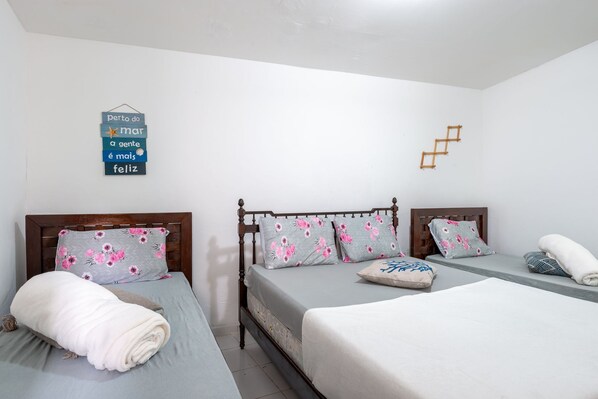 A hotel room with two beds, a wooden headboard, floral-patterned pillows, and a wall decoration with a Portuguese phrase.
