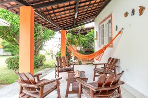 An outdoor seating area with wooden chairs and a table, a hammock, and a white wall with decorative items.