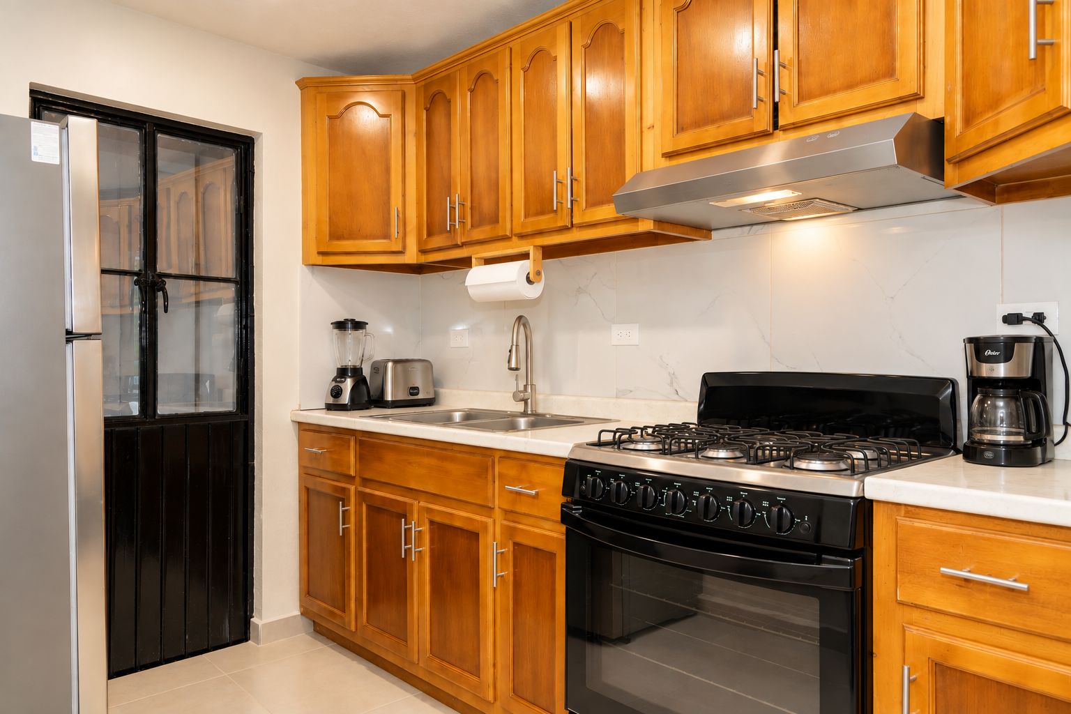 Una cocina con armarios de madera, un refrigerador de acero inoxidable, una estufa a gas y una cafetera.