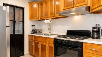 Una cocina con armarios de madera, un refrigerador de acero inoxidable, una estufa a gas y una cafetera.