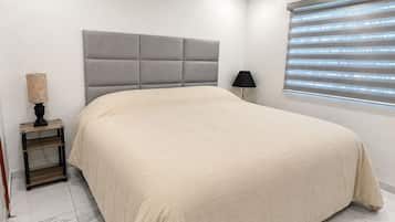 Un dormitorio con cama, ventilador de techo, mesita de noche, lámpara y ventana con persianas.