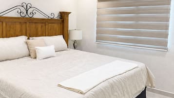 Un dormitorio con una cama, ventilador de techo, lámpara de noche y ventana con persianas.