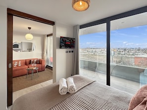 A modern hotel room with a large bed, a sofa, a TV, and a city view. - Nuevo - Metro - vista a la ciudad  (Santiago)