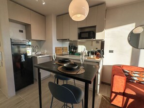 A modern kitchen with a central island, a dining area with a red sofa, and a microwave above the island. - Nuevo - Metro - vista a la ciudad  (Santiago)
