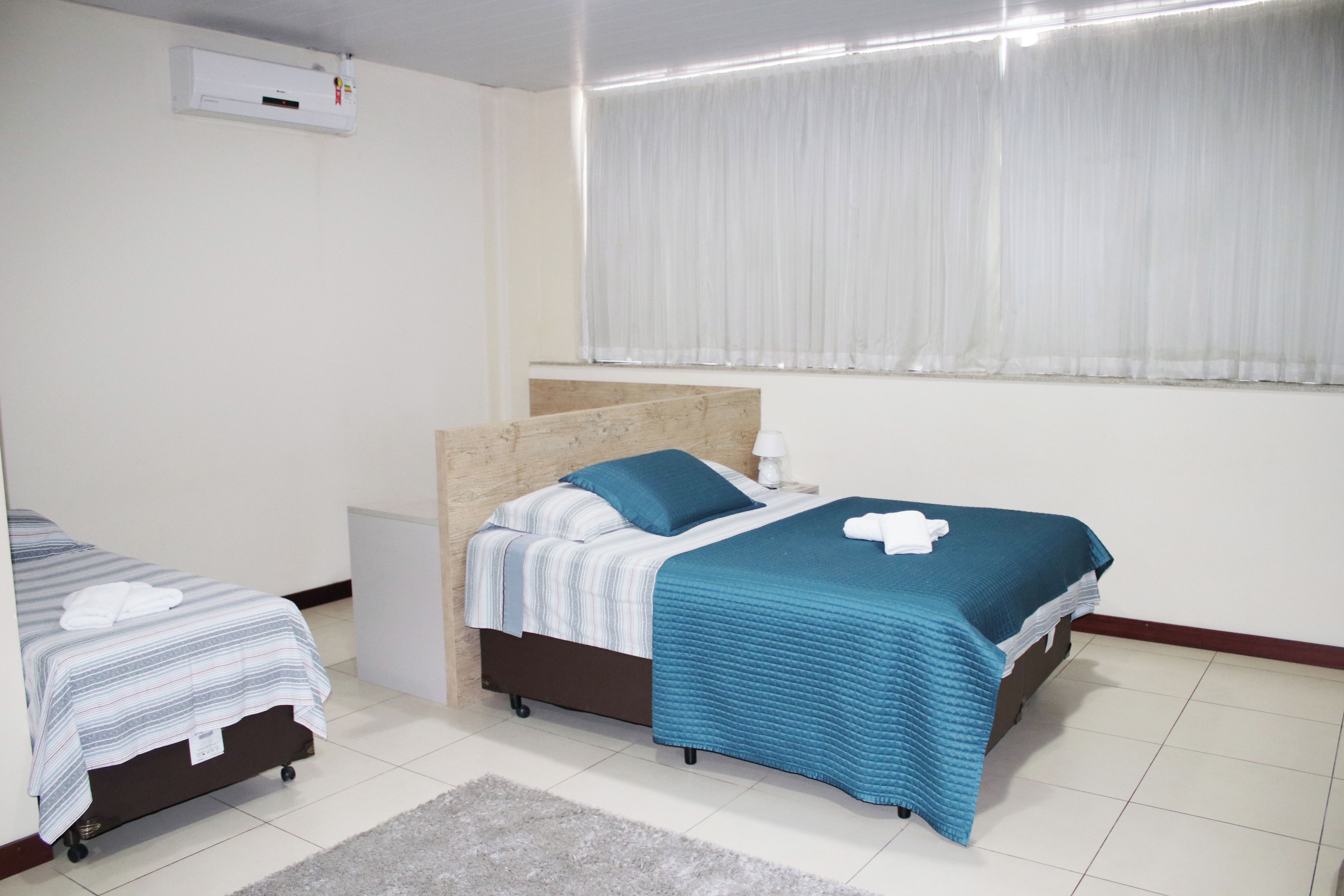 Een hotelkamer met twee bedden, een klein nachtkastje, gordijnen voor het raam en een wandairconditioner.