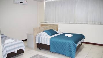 Een hotelkamer met twee bedden, een klein nachtkastje, gordijnen voor het raam en een wandairconditioner.