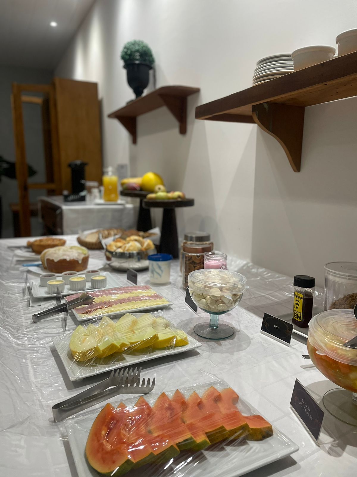 A buffet table with various food items, including sliced fruits and pastries, and a sign indicating the salad of fruits section.