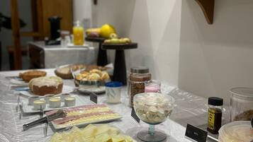 Une table de buffet proposant divers aliments, notamment des fruits coupés et des pâtisseries, ainsi qu’un panneau indiquant l’emplacement de la section des salades de fruits.