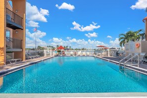 A clear blue pool with a flag, lounge chairs, and umbrellas. - Boca Shores 123 (St. Pete Beach)