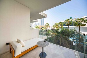 A balcony with a sofa and a small table, overlooking a cityscape with palm trees and modern buildings. - Modern 2BR Gem | Prime Palm Jumeirah Location (Dubai)