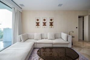 A modern living room with a white sofa, a glass coffee table, and abstract wall art. - Modern 2BR Gem | Prime Palm Jumeirah Location (Dubai)